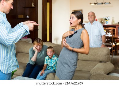 Portrait Of Young Outraged Woman Emotionally Talking To Man On Background With Anxious Senior Parents And Tween Boy