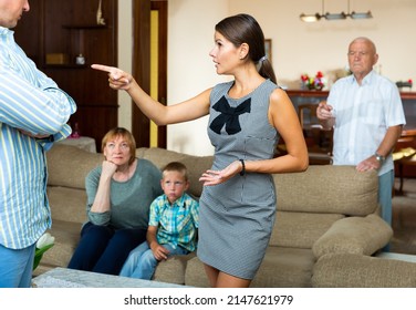 Portrait Of Young Outraged Woman Emotionally Talking To Man On Background With Anxious Senior Parents And Tween Boy