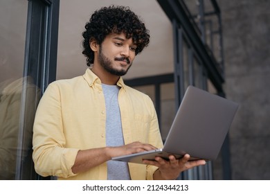 Portrait of young pensive Indian businessman using laptop computer working online in modern office. Handsome programmer working freelance project. Asian student studying at home, online education 