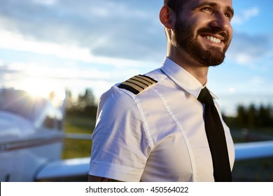 Portrait von jungen Piloten in Uniform posiert mit einem glücklichen Zahnlächeln mit Flugzeugen auf dem Hintergrund. Sonniges Hintergrundfoto