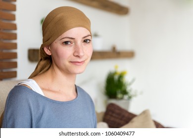 Portrait Of Young Positive Adult Female Cancer Patient Sitting In Living Room, Smiling And Looking At The Camera.