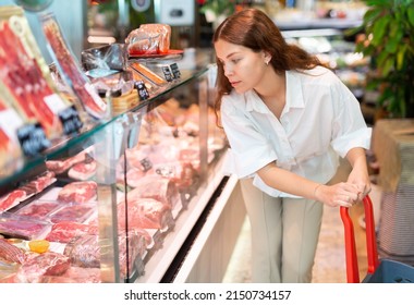 Portrait of young positive woman shopping at grocery department of supermarket, choosing raw meat products - Powered by Shutterstock