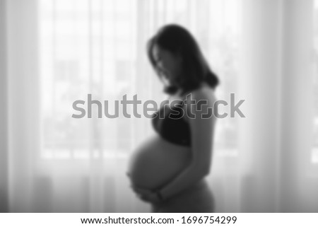 Portrait of young pregnant attractive woman, standing by the window ,out of focus in blackandwhite tone