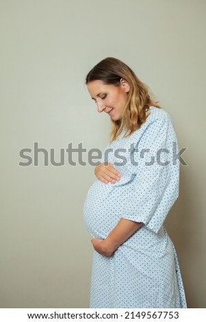 Portrait of a young pregnant woman in hospital robe holding big belly profile view