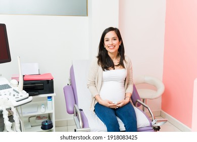 Portrait of a young pregnant woman smiling and sitting on the examination chair in a doctor's office. Expectant mother waiting for her gynecologist