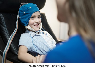Portrait of young preteen autistic girl smiling and looking at camera, while medical staff performs EEG in hospital laboratory. The girl smiles while doing electroencephalogram