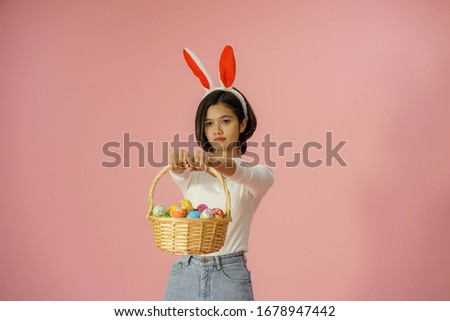 the portrait of young pretty Asian chinese happy smiling  Thai woman carrying the colorful Easter eggs basket celebrating the traditonal festival on pink background