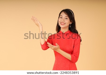Portrait of a young pretty beautiful woman in Vietnamese traditional outfit, isolated on background, with hand gesture. Concept of Lunar New Year (Tet holiday)