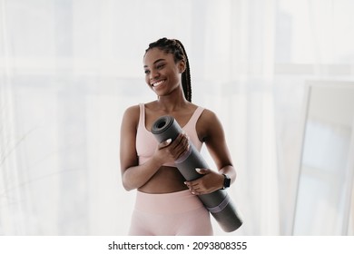 Portrait Of Young Pretty Black Woman In Sportswear Holding Fitness Mat, Posing And Smiling At Home Gym. Millennuial African American Lady Ready For Yoga Or Pilates Class, Indoors