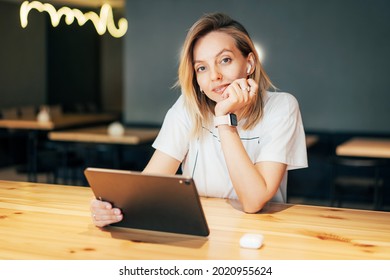 Portrait Of A Young Pretty Blonde Woman Looking At The Camera While Sitting In A Cafe With A Tablet