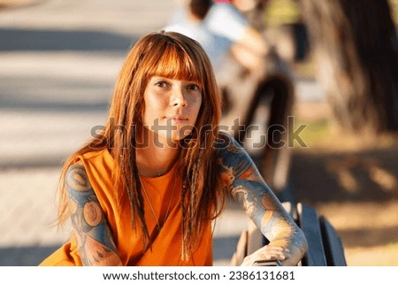 Portrait of young pretty Caucasian woman with tattoos poses sitting on bench. Concept of psychology.