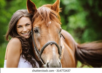 Portrait of young pretty cheerful woman with horse at summer green park.