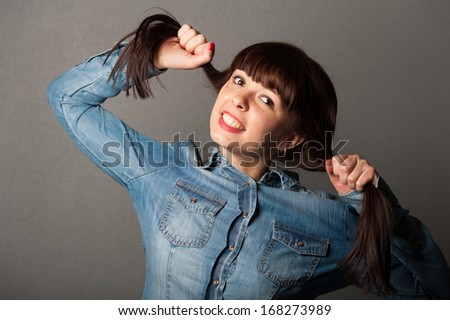Portrait of young pretty cute girl holding her brown hairs on grey background