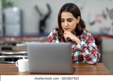 Portrait Of A Young Pretty Indian Woman Working On Her Laptop, Sitting In An Office Cafeteria, Coffee Shop, Casual Work Environment.