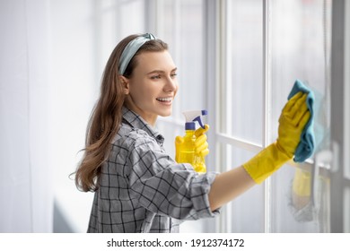 Portrait Of Young Pretty Lady In Rubber Gloves Cleaning Window With Detergent At Home. Lovely Millennial Housewife Keeping Her Home Tidy, Happily Performing Domestic Chores, Enjoying Housework