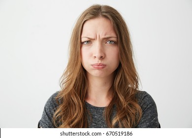 Portrait of young pretty offended girl with funny face looking at camera frowning over white background.