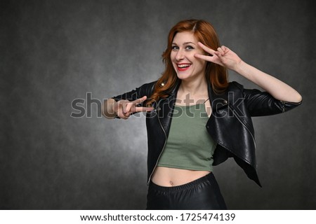 Portrait of a young pretty woman with beautiful hair and excellent make-up in a green T-shirt and a black jacket on a gray background. The model demonstrates vivid emotions by changing poses.