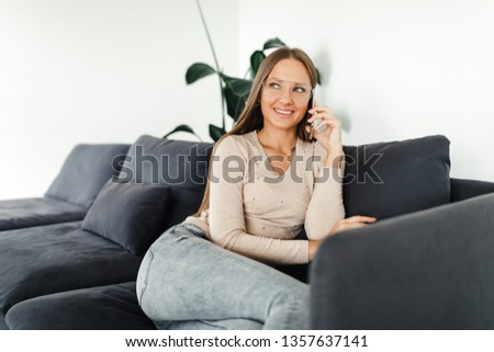 Portrait of a young pretty woman in glasses talking over the phone while sitting on the couch at home