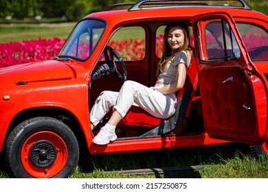 Portrait of young pretty woman leaning over rustic cabriolet car in colorful tulip fields. Chilliwack Tulip Ftstival. British Columbia. Canada