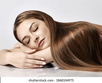 Portrait of young pretty woman model with silky long straight hair lying and relaxing with eyes closed over white background. Hairstyle, hairsalon, hairdresser, fashion concept