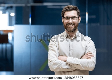 Portrait of a young programmer and engineer standing in the office with his arms crossed on his chest and smiling at the camera.