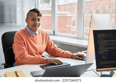 Portrait of young programmer smiling at camera while working with security codes on computer sitting at his workplace