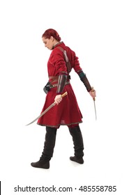 Portrait Of A Young, Red Haired  Female Warrior,  Wearing A Red Medieval Tunic And Leather Armour.  Isolated On A White Background Holding  A Weapon.