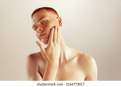 Portrait of young red-haired man with freckles touching cheeks, posing isolated over grey studio background. After shaving. Concept of men's health, lifestyle, beauty, body and skin care - Powered by Shutterstock