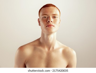 Portrait of young red-haired man posing shirtless isolated over grey studio background. Freckled face. Concept of men's health, lifestyle, beauty, body and skin care. Model looking at camera