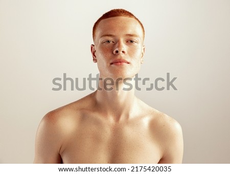 Portrait of young red-haired man posing shirtless isolated over grey studio background. Freckled face. Concept of men's health, lifestyle, beauty, body and skin care. Model looking at camera