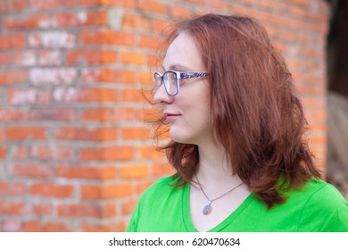 Portrait of a young red-haired woman in green t-shirt standing by the brick wall - Powered by Shutterstock