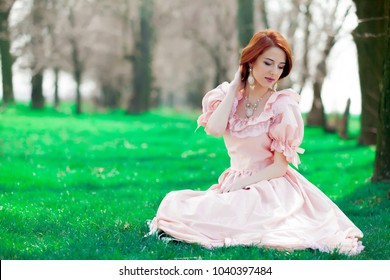 Portrait Of A Young Redheadd Girl In Victorian Style Dress Sitting On Grass In Springtime 