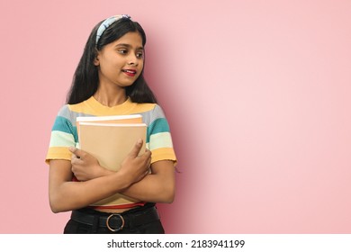 Portrait of young relaxed indian asian girl posing isolated looking away at copyspace and hugging books expressing positive emotions and calmness.