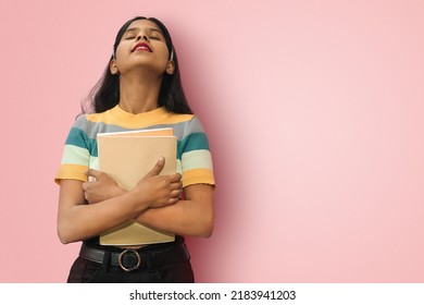 Portrait of young relaxed indian asian girl posing isolated tilting head backwards and hugging books expressing positive emotions and calmness. Mock up copy space