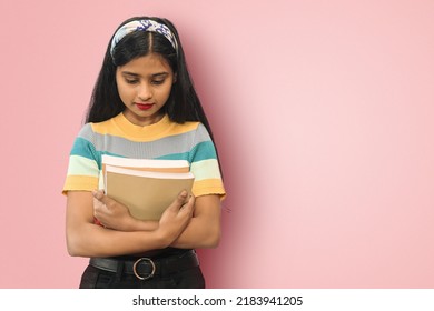Portrait of young relaxed indian asian girl posing isolated tilting head forward down looking downwards and hugging books expressing positive emotions and calmness. Mock up copy space