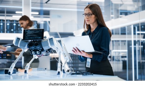 Portrait of a Young Robotics Engineer Using Laptop Computer, Analyzing Robotic Machine Concept in a High Tech Factory. Female Scientist Manipulate and Program the Robot for Work. - Powered by Shutterstock