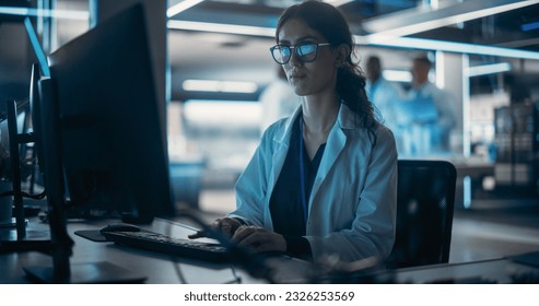 Portrait of a Young Robotics Engineer Using Desktop Computer, Analyzing Robotic Machine Concept in a High Tech Factory. Female Scientist Researching Innovative Ways to Benefit and Progress Humanity