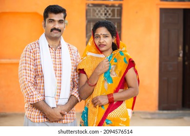 Portrait of young rural indian couple standing outdoor at village house. Mustache man wearing kurta and woman wearing sari, husband wife wearing traditional cloths looking at camera. - Shutterstock ID 2094576514