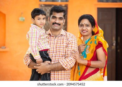 Portrait of young rural indian family standing outdoor at village house. Parent holding their little child, Mustache man wearing kurta and woman wear sari, Couple wearing traditional cloths with kid - Shutterstock ID 2094575452