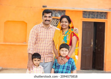 Portrait of young rural indian family standing with their two little children boys outdoor at village house. Mustache man wearing kurta and woman wearing sari, husband wife wearing traditional cloths.