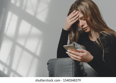 Portrait of a young sad crying girl with a smartphone in her hand, as a symbol of the negative impact of technology on the human psyche or unsuccessful relationships.
