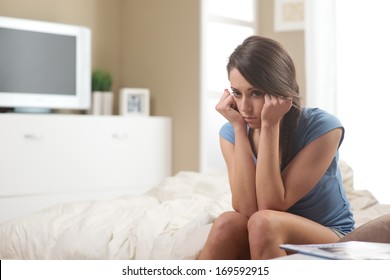 Portrait Of Young Sad Woman Sitting On Bed