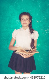 Portrait of a young schoolgirl in the form of extravagant with a briefcase or backpack. Read old books, bright emotion on her face. Vintage toning, Rustic. Green background