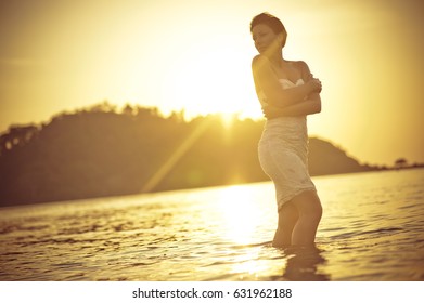 Portrait of a young and sensual woman walking in the water of a tropical beach at sunset