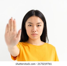 Portrait Of Young Serious Asian Woman Showing Stop Gesture And Looking At Camera On A White Background