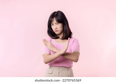 portrait young serious asian woman with cross arm gesture showing stop, no, wrong, denial, rejection sign isolated on pink pastel studio background. deny and negative expression symbol concept. - Shutterstock ID 2270765369