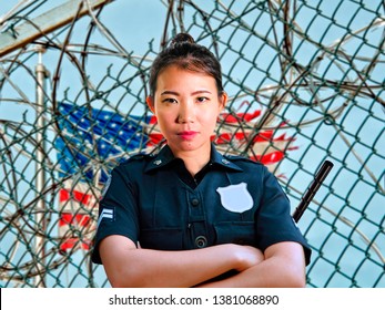 Portrait Of Young Serious And Attractive Asian American Guard Woman Standing At State Penitentiary Prison Barbwire Fence Wearing Police Uniform In Crime Punishment And Law Concept