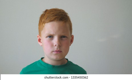 Portrait Of Young Serious Red-haired Boy With Freckles Inside. Adorable Handsome Kid Looking Into Camera Indoor. Close Up Emotions Of Little Male Child With Sad Expression On Face. Slow Motion