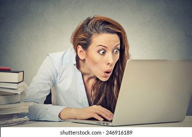 Portrait young shocked business woman sitting in front of laptop computer looking at screen isolated grey wall background. Funny face expression emotion feelings problem perception reaction 