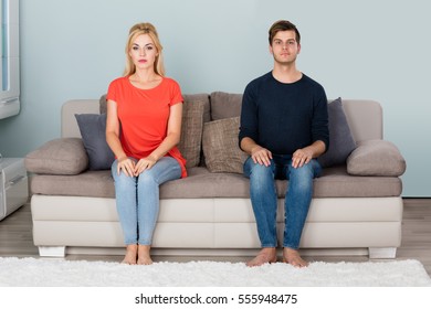 Portrait Of Young Shy Couple Sitting On Sofa At Home